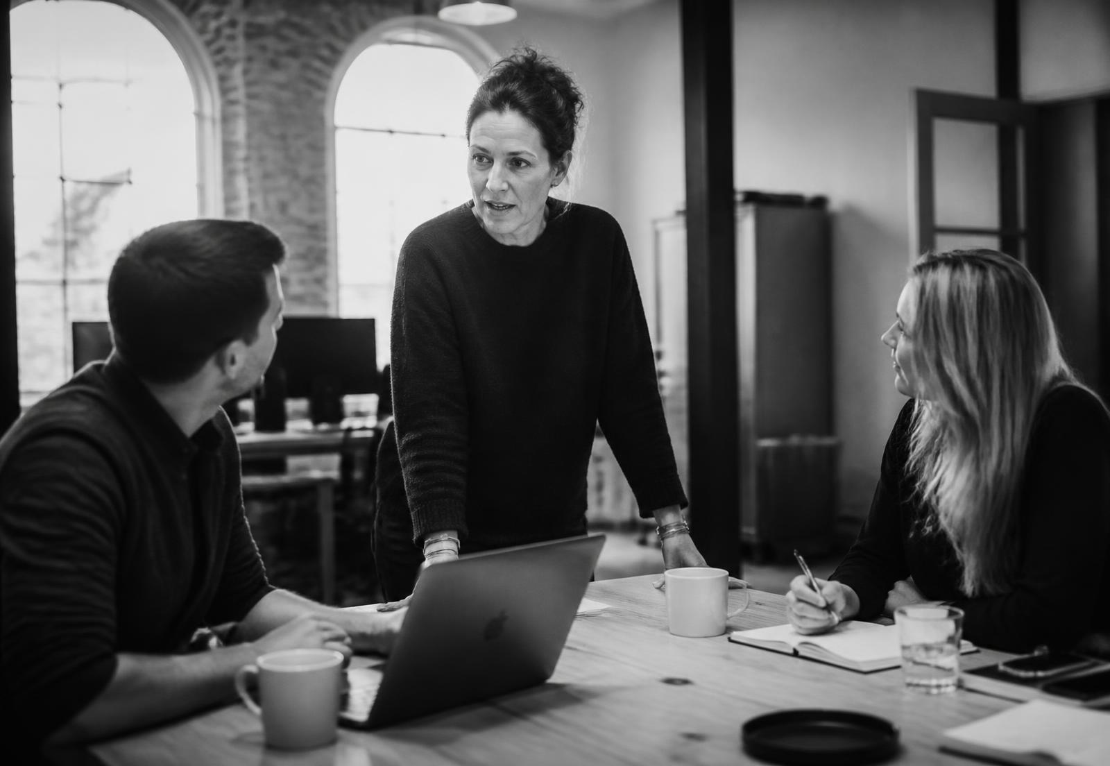 A founder in conversation with two colleagues around a table in a converted warehouse studio